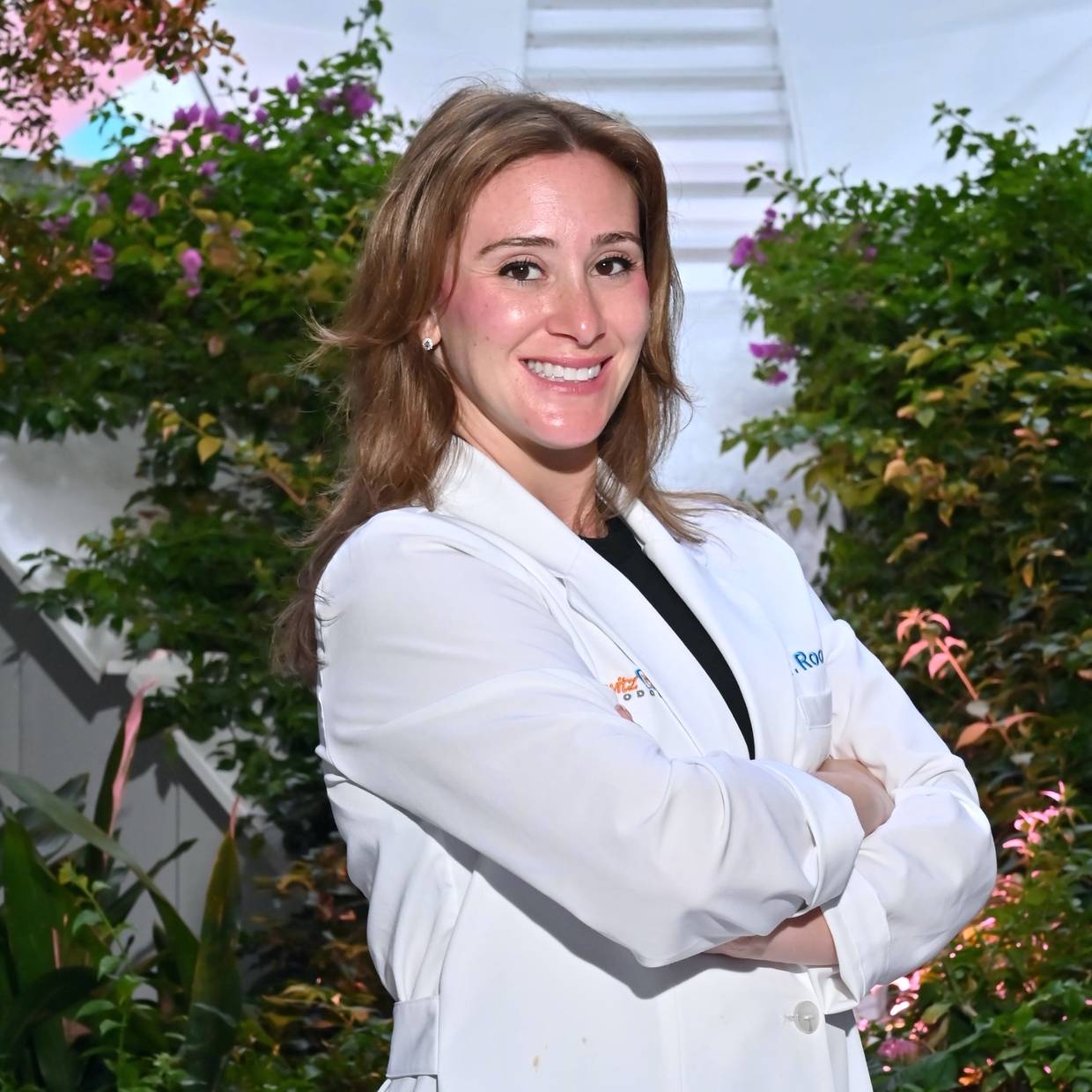 Dr. Shannon Rooney, orthodontist at Sakowitz Smiles, smiling in her white coat with arms crossed